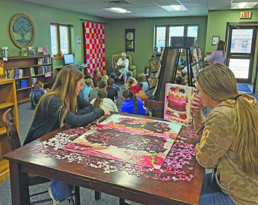 Callaway Public School paras Katie Mason (left) and Keegan Mehrens work a puzzle while the older group attending Nigel Sprouse Memorial Library's Summer Reading Program listen to the featured book being read by board president and retired school librarian, Judy Reiff.