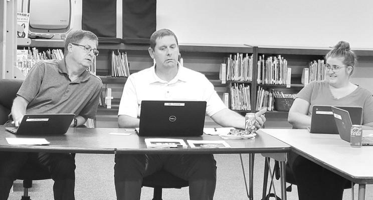 Callaway school board president Mike Reiff, left, assists new Superintendent JD Furrow with logging on for his first board meeting on July 8. Pictured to right of Mr. Furrow is the board's newest member, Rebecca Eggleston. (Courier photo by Ellen Mortensen)