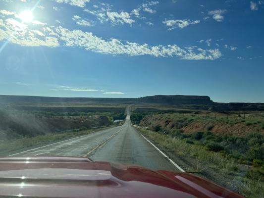 An open road surrounded by low green hills and a bright blue sky.