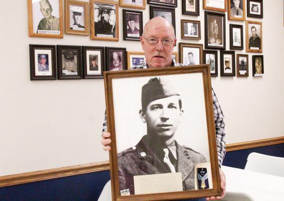 Callaway American Legion Post 59 Adjutant Bill Schaad holds the portrait of WW II Army Private Robert D. Booker that proudly hangs in the Legion Hall. Booker has been immortalized as a war hero for his actions protecting his comrades under enemy fire. (Courier photo by Ellen Mortensen)